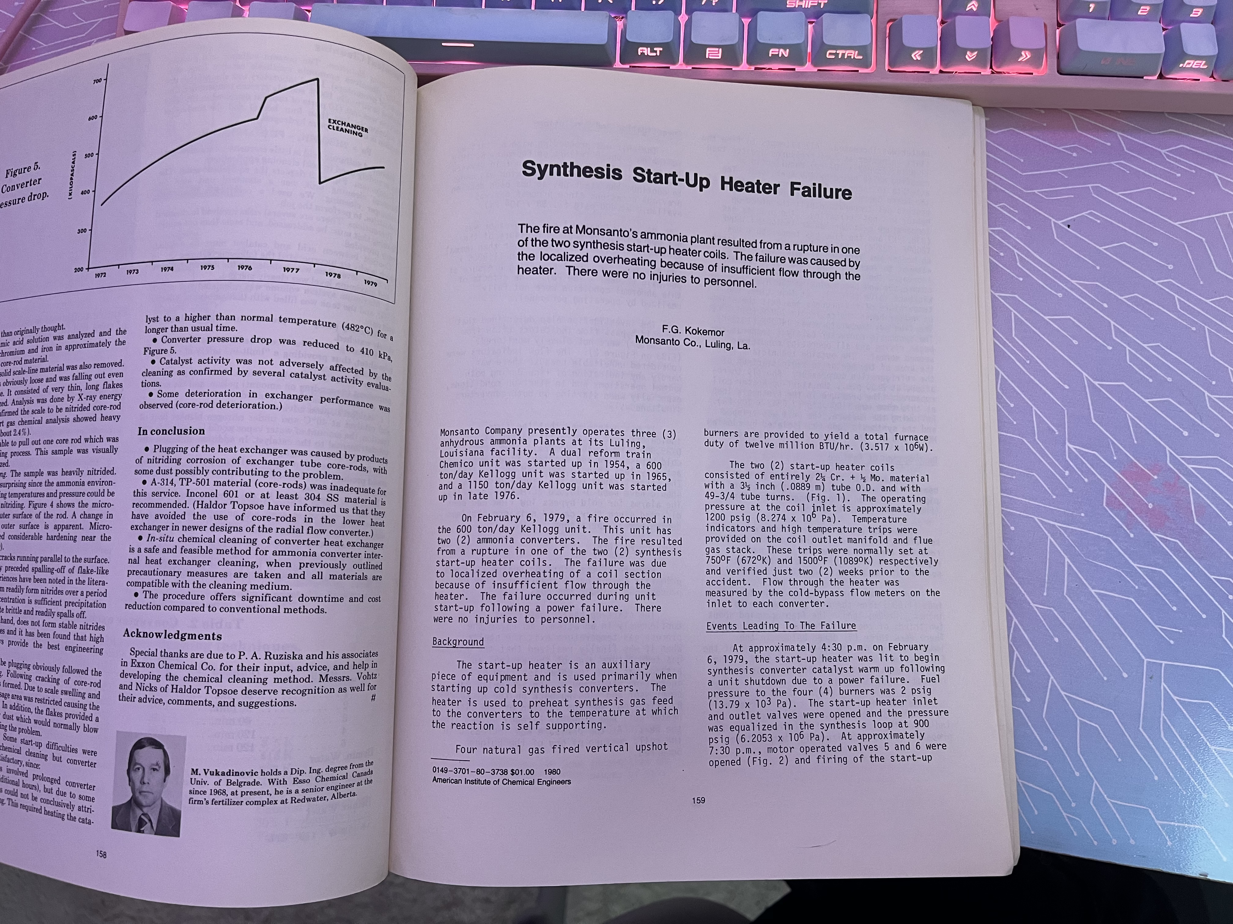 A photograph of the article “Synthesis Start-Up Heater Failure” on top of my custom desk by Chassie, which features a circuit-board meets magic runes design in pastel shades of pink, purple, and blue. My matching keyboard is barely visible in the top part of the photograph. The synopsis of the article reads: “The fire at Monsanto’s ammonia plant resulted from a rupture in one of the two synthesis start-up heater coils. The failure was caused by the localized overheating because of insufficient flow through the heater. There were no injuries to personnel.”